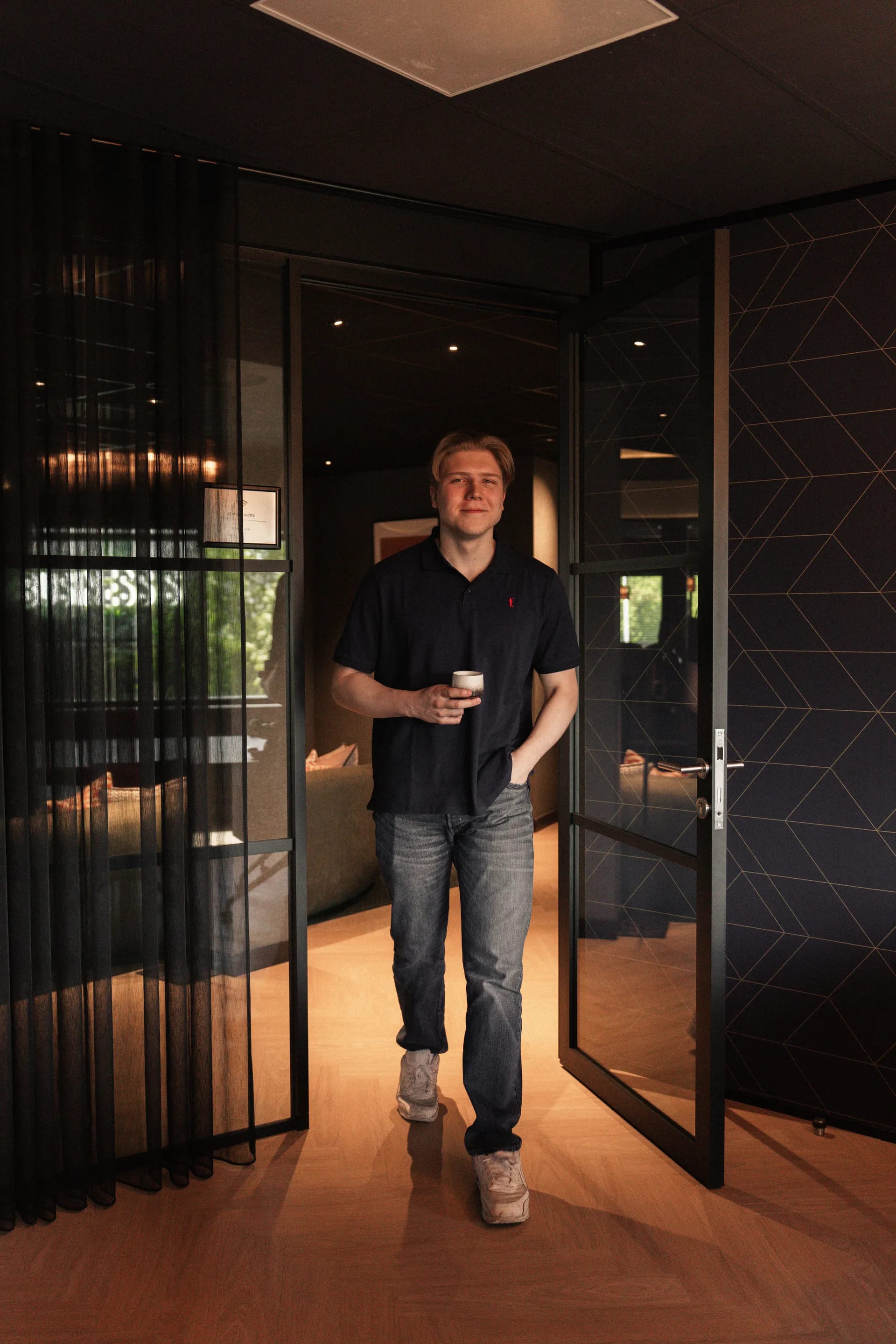 Jesse loopt met een kop koffie door de deuropening